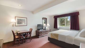A hotel room with a bed, a desk with a chair, a television, a dresser, and a window with curtains.