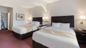 A hotel room with two beds, a nightstand with a lamp, a telephone, and a framed picture on the wall.