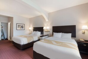 A hotel room with two beds, a nightstand with a lamp, a telephone, and a framed picture on the wall.