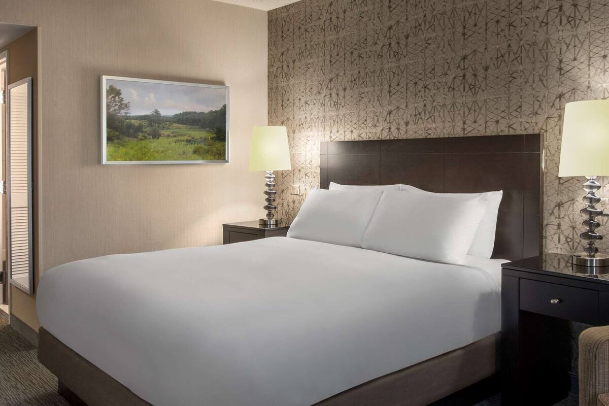 A hotel room with a large bed, two bedside tables with lamps, a chair, and a patterned wallpaper.
