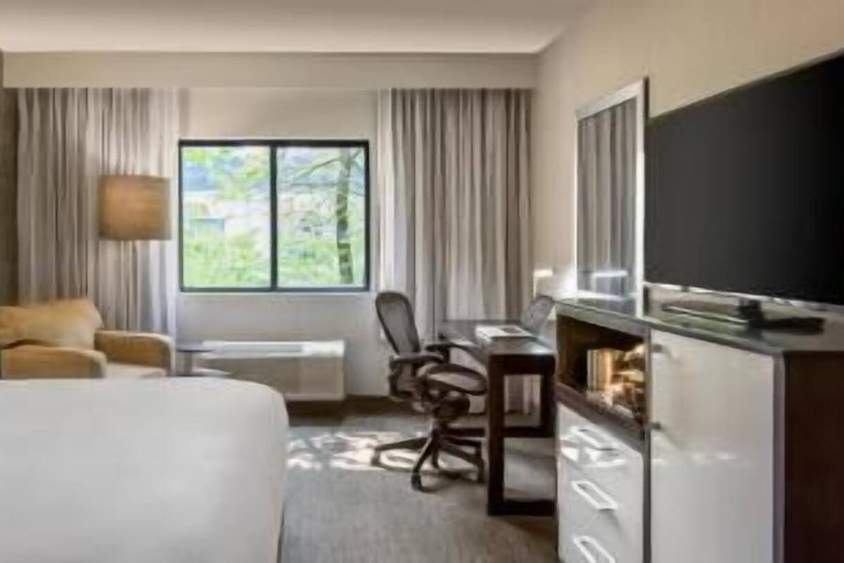 A hotel room with a bed, a desk, a chair, a television, and a window with curtains.
