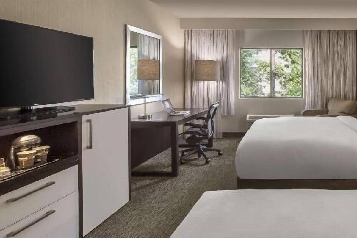 A hotel room with a bed, a desk, a television, and a window with curtains.
