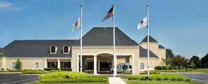 A building with a beige facade, a dark roof, and a central entrance with columns. There are two flags on flagpoles in front. - DoubleTree by Hilton Hotel Chicago Wood Dale - Elk Grove (Wood Dale)