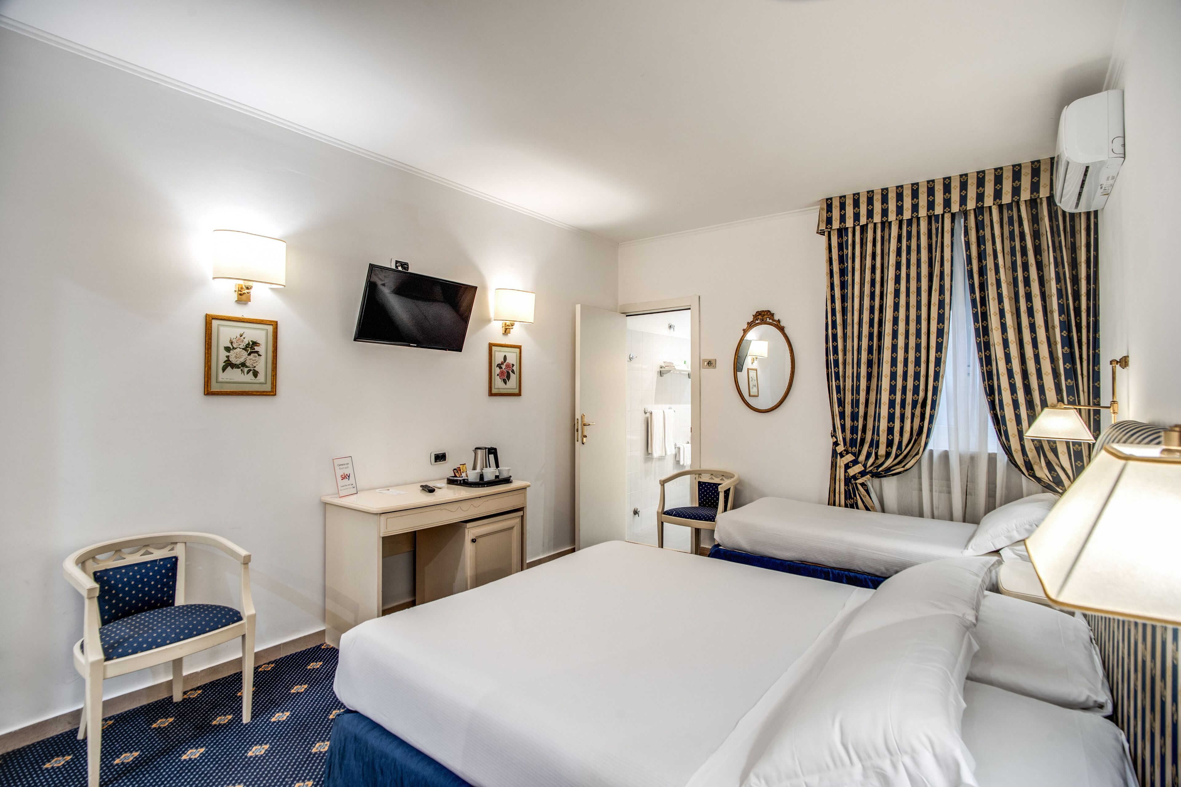 Habitación de hotel con dos camas, un escritorio, una silla, un televisor y la puerta del baño.