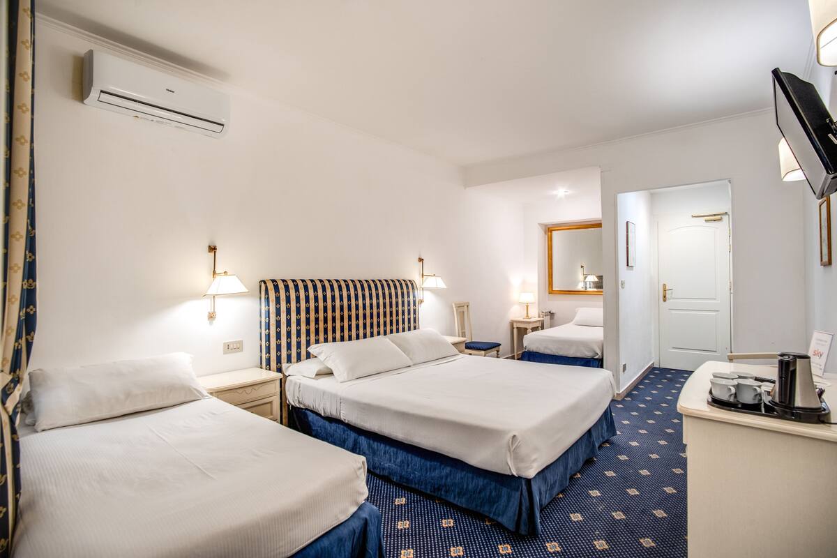 Habitación de hotel con dos camas, un escritorio con cafetera, televisión y aire acondicionado.