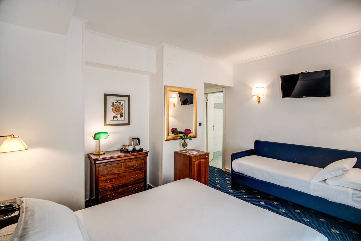 Una habitación de hotel con una cama grande, una cama más pequeña, un aparador, un espejo, un televisor y una lámpara.