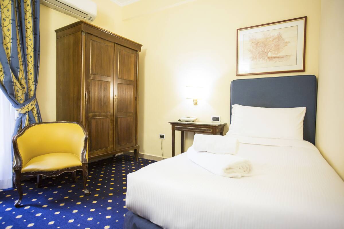 Una habitación de hotel con cama, armario de madera, una silla y escritorio con lámpara.