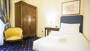 A hotel room with a bed, a wooden wardrobe, a chair, and a desk with a lamp.