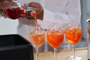Eine Person gießt eine rote Flüssigkeit in drei Gläser mit Eiswürfeln.