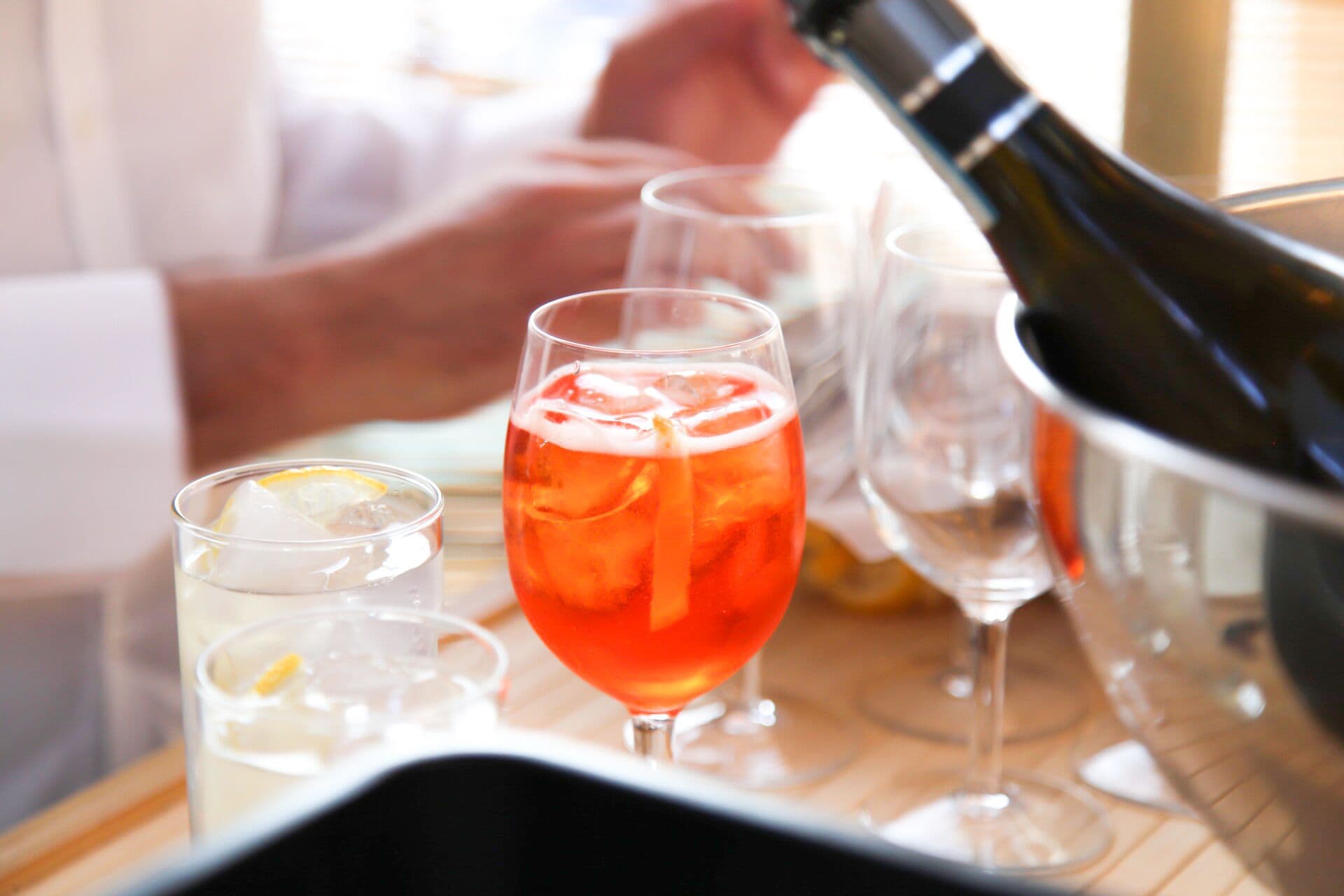A bar setting with a bottle of champagne, a glass of red drink, and a glass of white drink with a lemon slice.