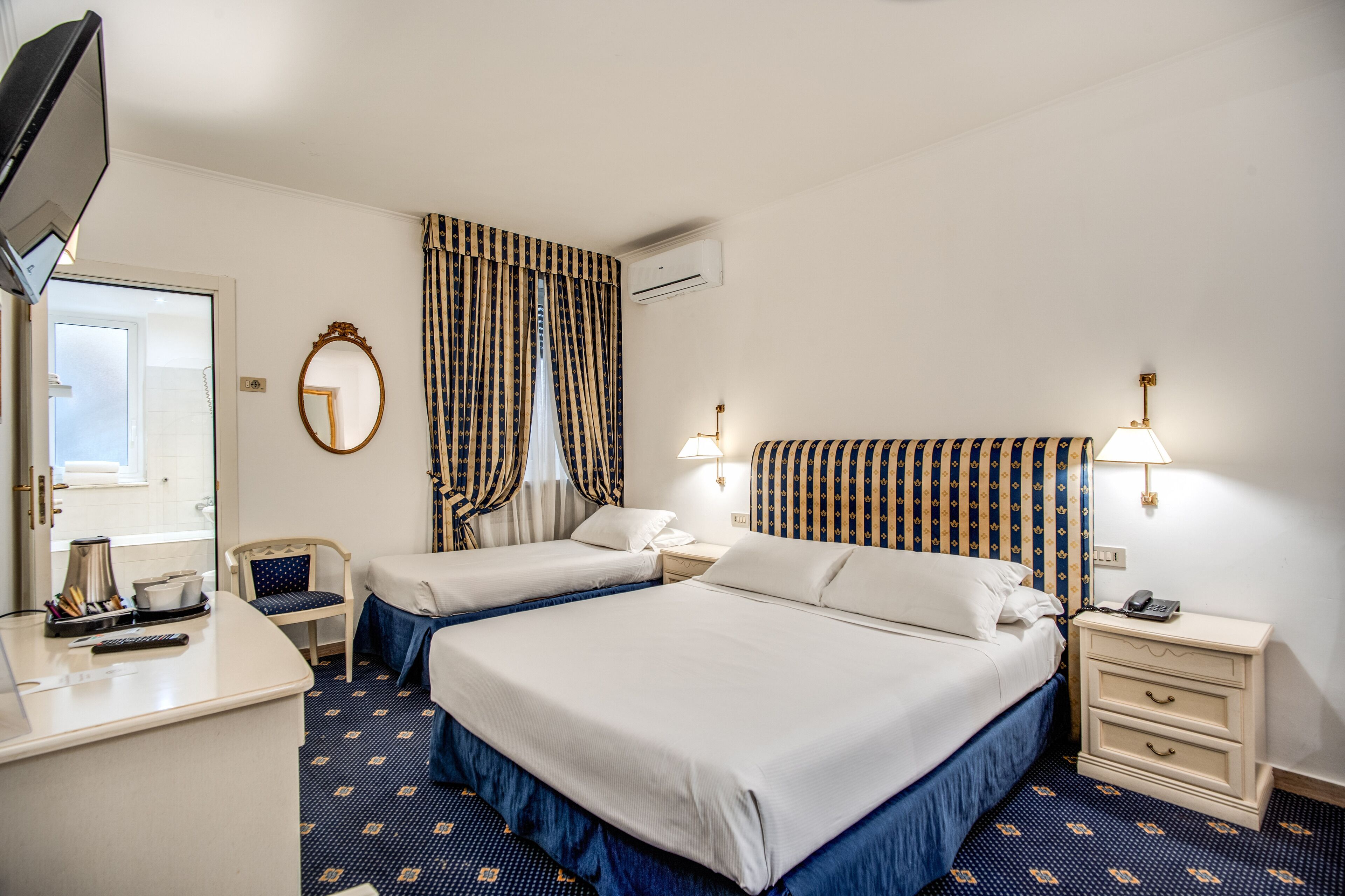 Ein Hotelzimmer mit zwei Betten, einem Schreibtisch, einem Stuhl, einem Spiegel und einem Fernseher.