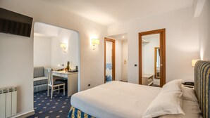 Habitación de hotel con cama, escritorio, silla, espejo y televisor instalado en la pared.