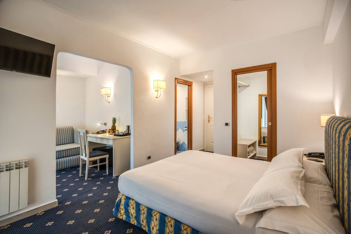 Habitación de hotel con cama, escritorio, silla, espejo y televisor instalado en la pared.