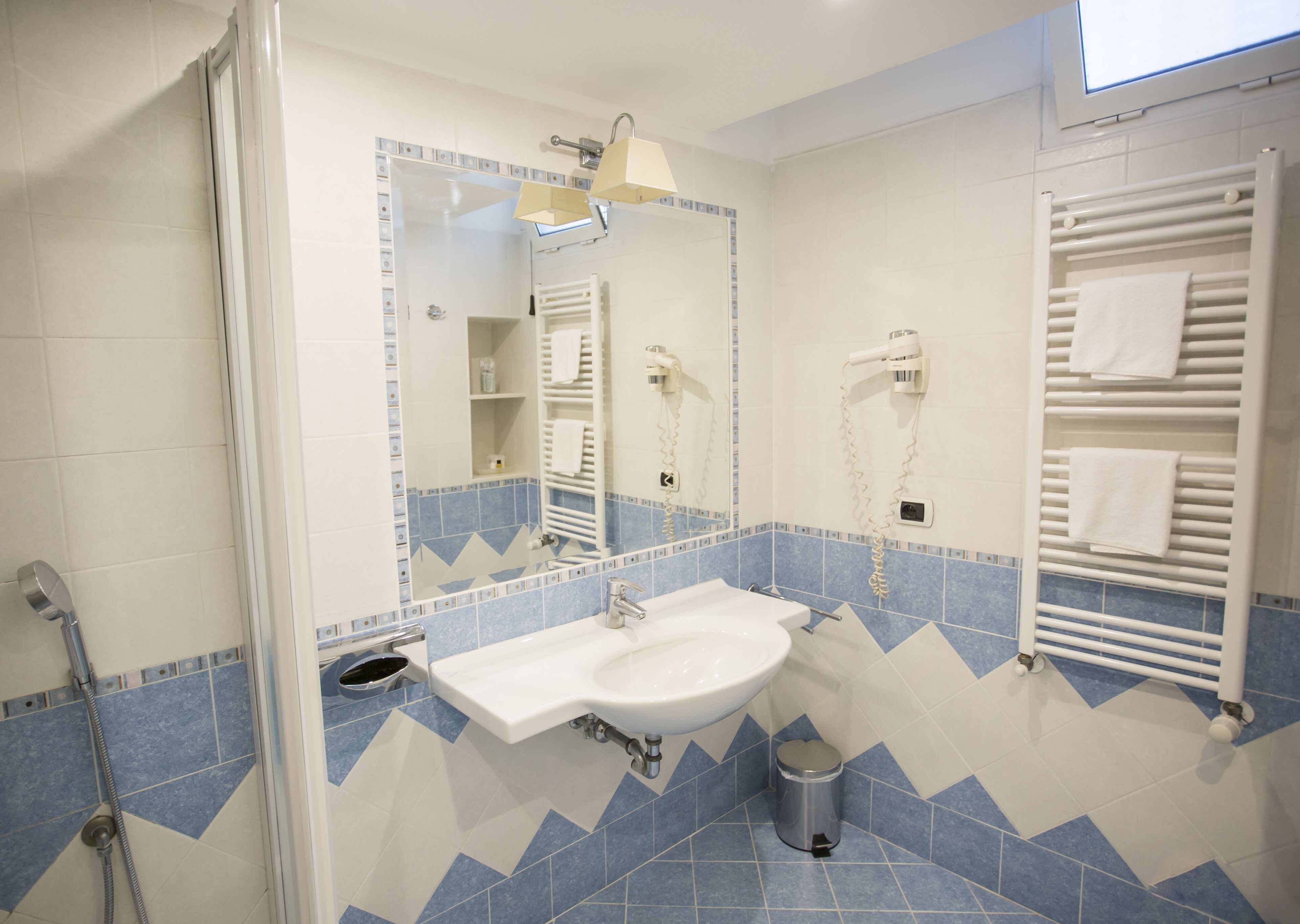 A bathroom with a sink, mirror, towel rack, and shower.
