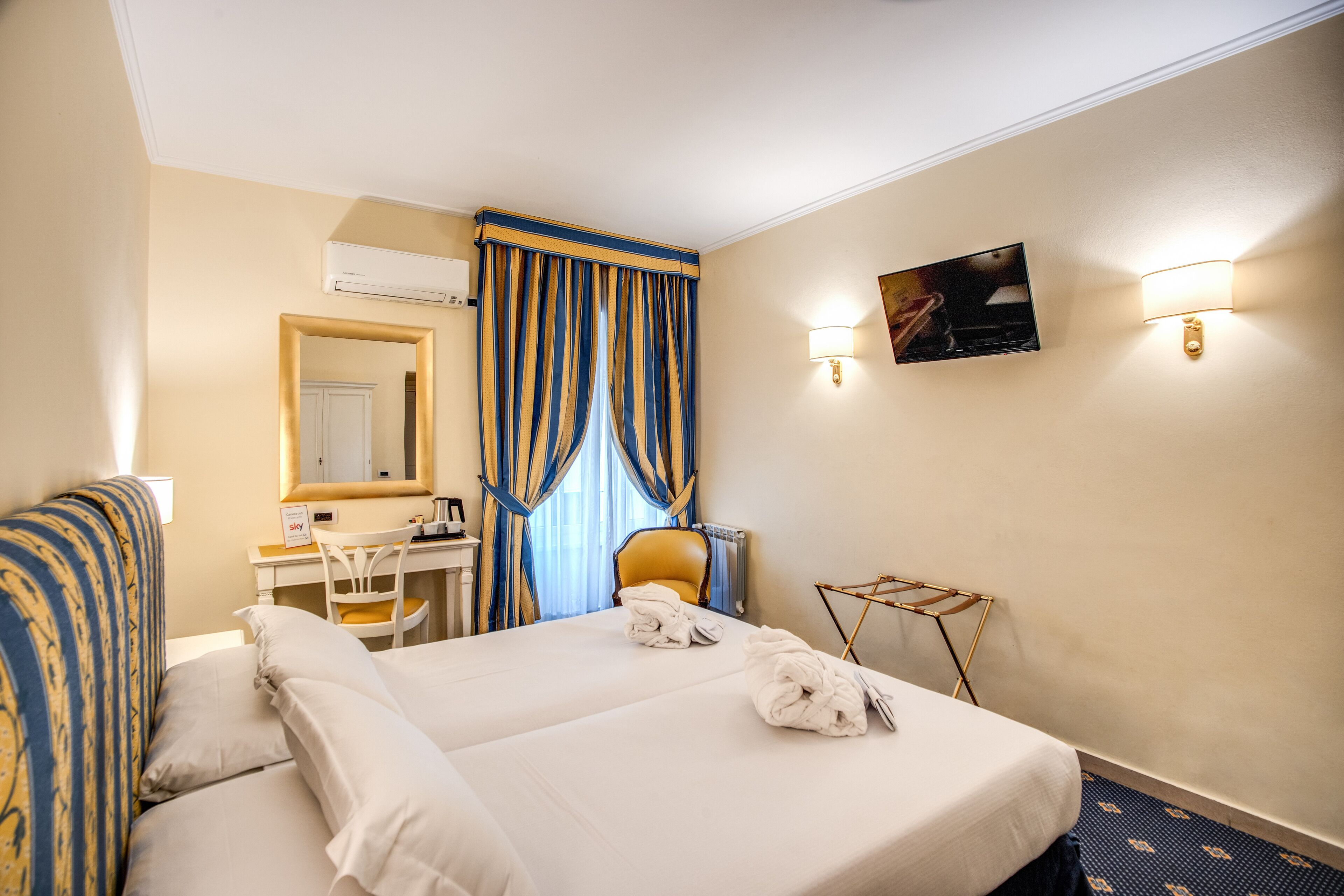Une chambre d’hôtel équipée d’un lit, d’un bureau, d’une chaise, d’un miroir et d’un téléviseur fixé au mur.