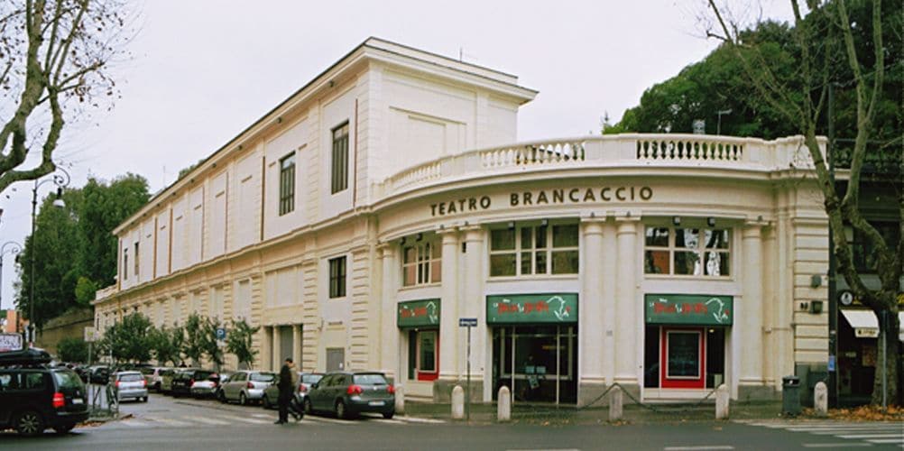 Ein historisches Gebäude mit einer klassischen Fassade, mit der Aufschrift „Teatro Brancaccio“, das einen prachtvollen Eingang und mehrere Geschäfte aufweist.
