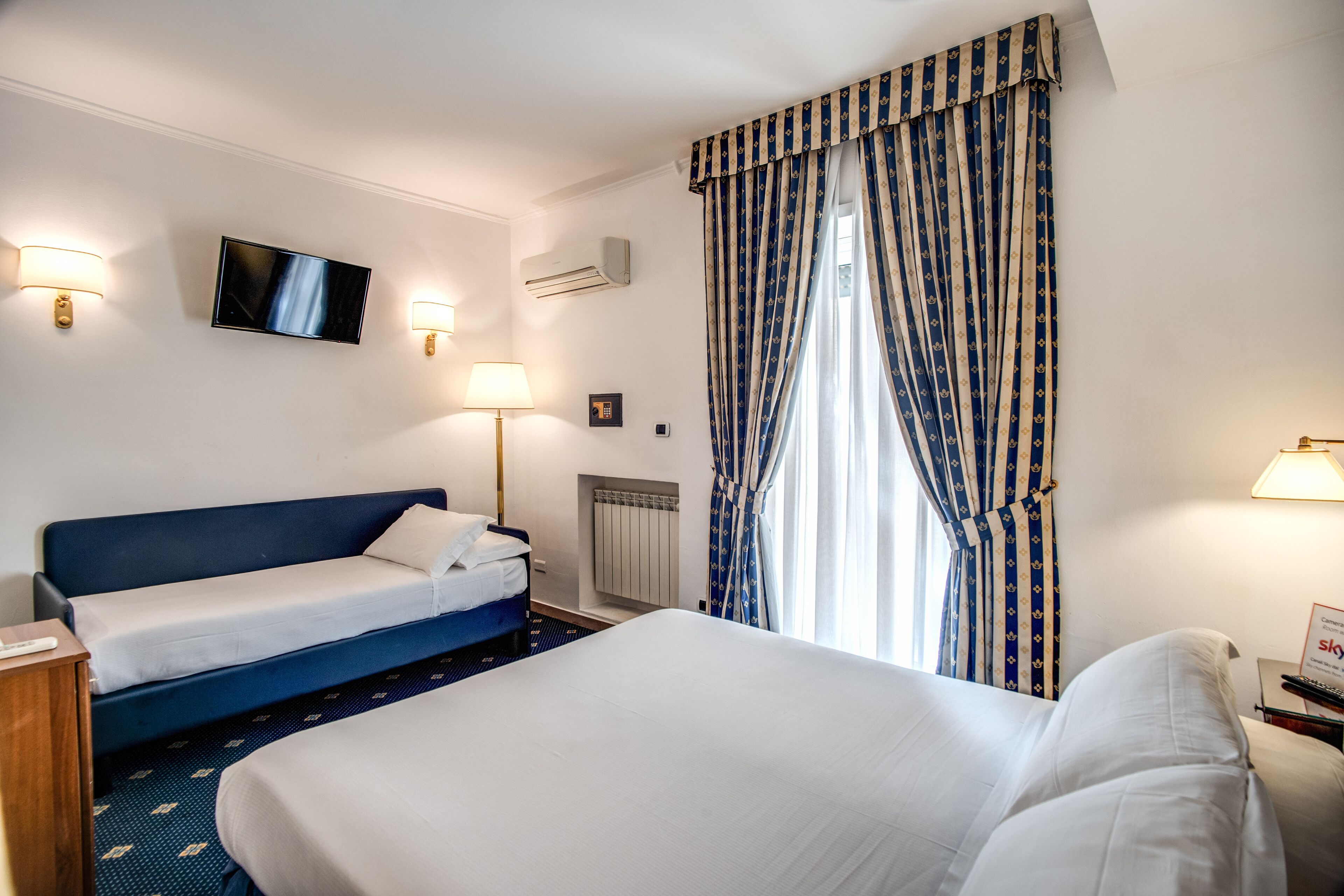 Una camera d'albergo con un letto grande, un letto più piccolo, una TV e due lampade da comodino.
