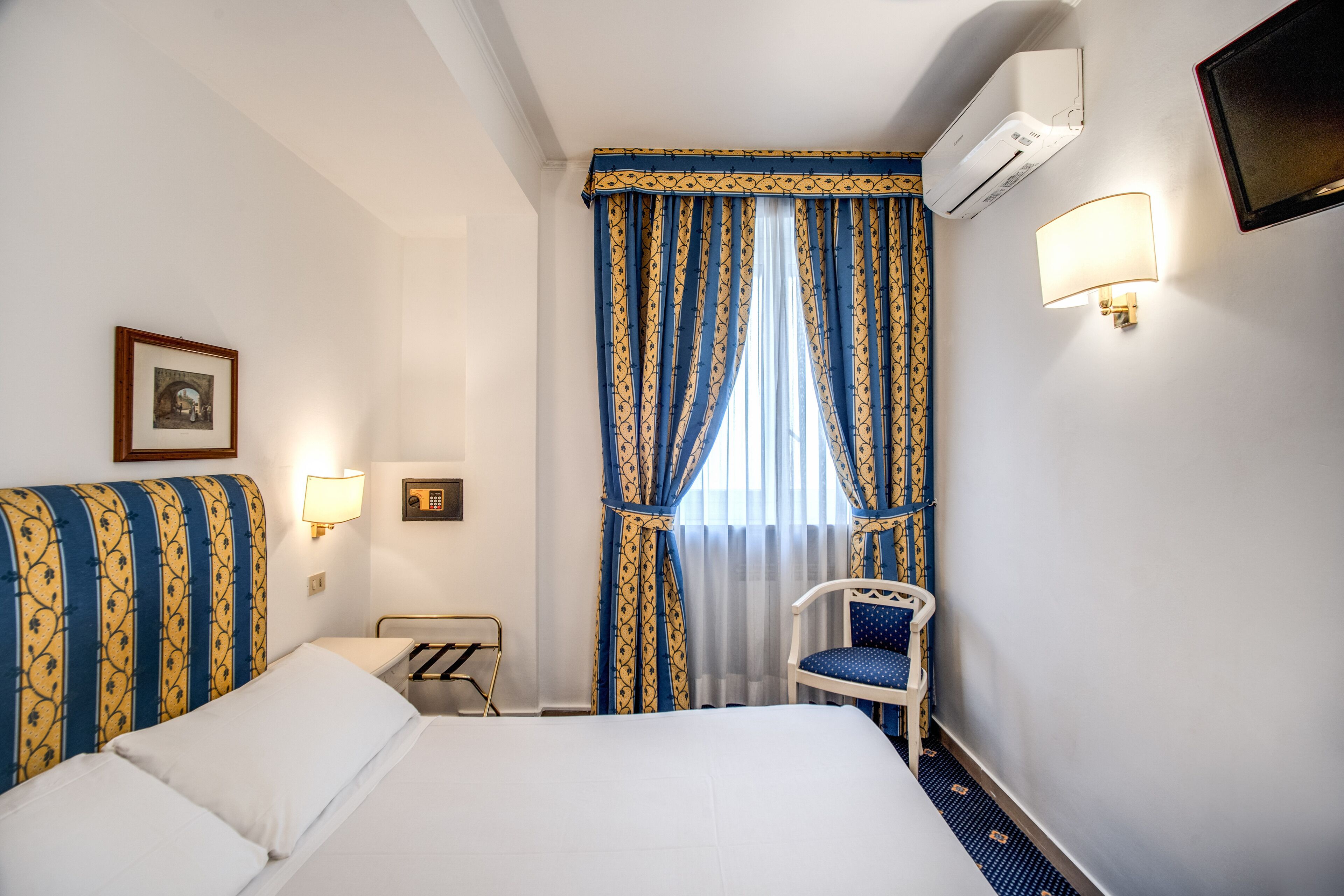 Ett hotellrum med en säng, en stol, ett skrivbord och ett fönster med gardiner.