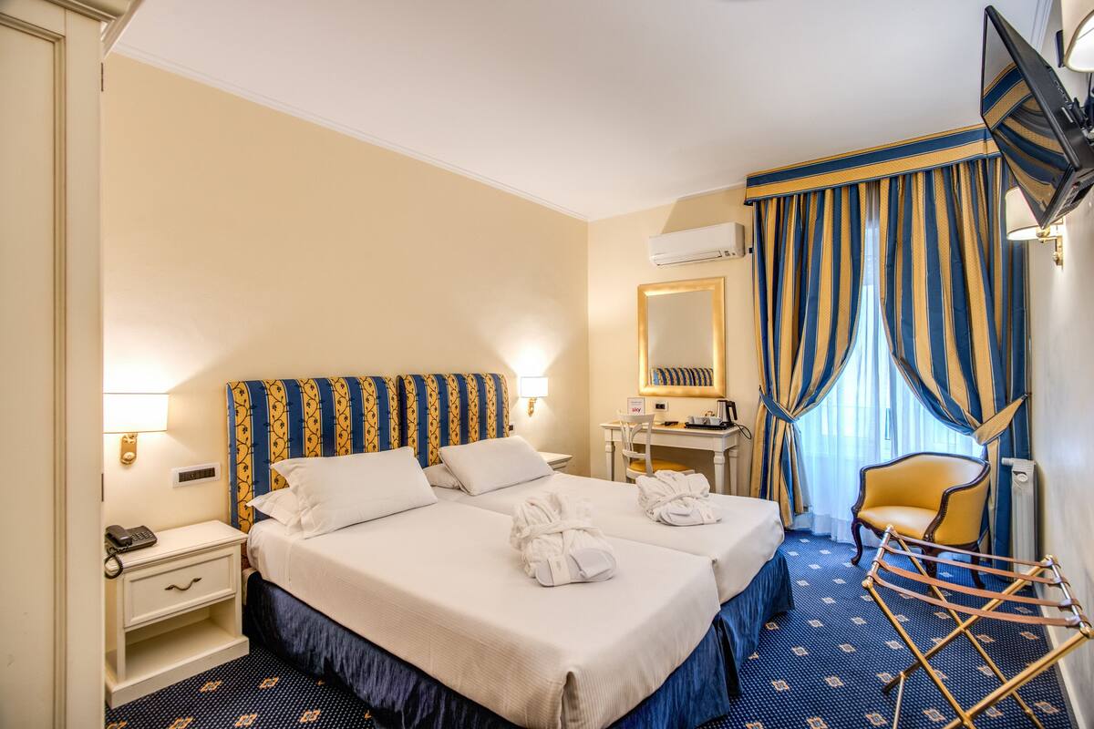 Una habitación de hotel con dos camas, un escritorio, una silla y un televisor.