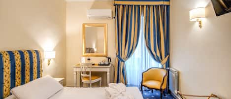 Quarto de hotel com cama, escrivaninha, cadeira e televisão.