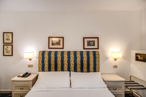 A hotel room with a bed, two bedside tables, a telephone, and framed pictures on the wall.