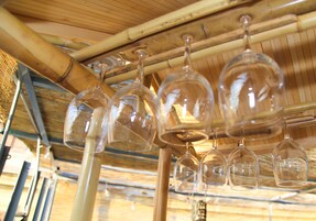 A row of wine glasses hanging from a bamboo ceiling structure.