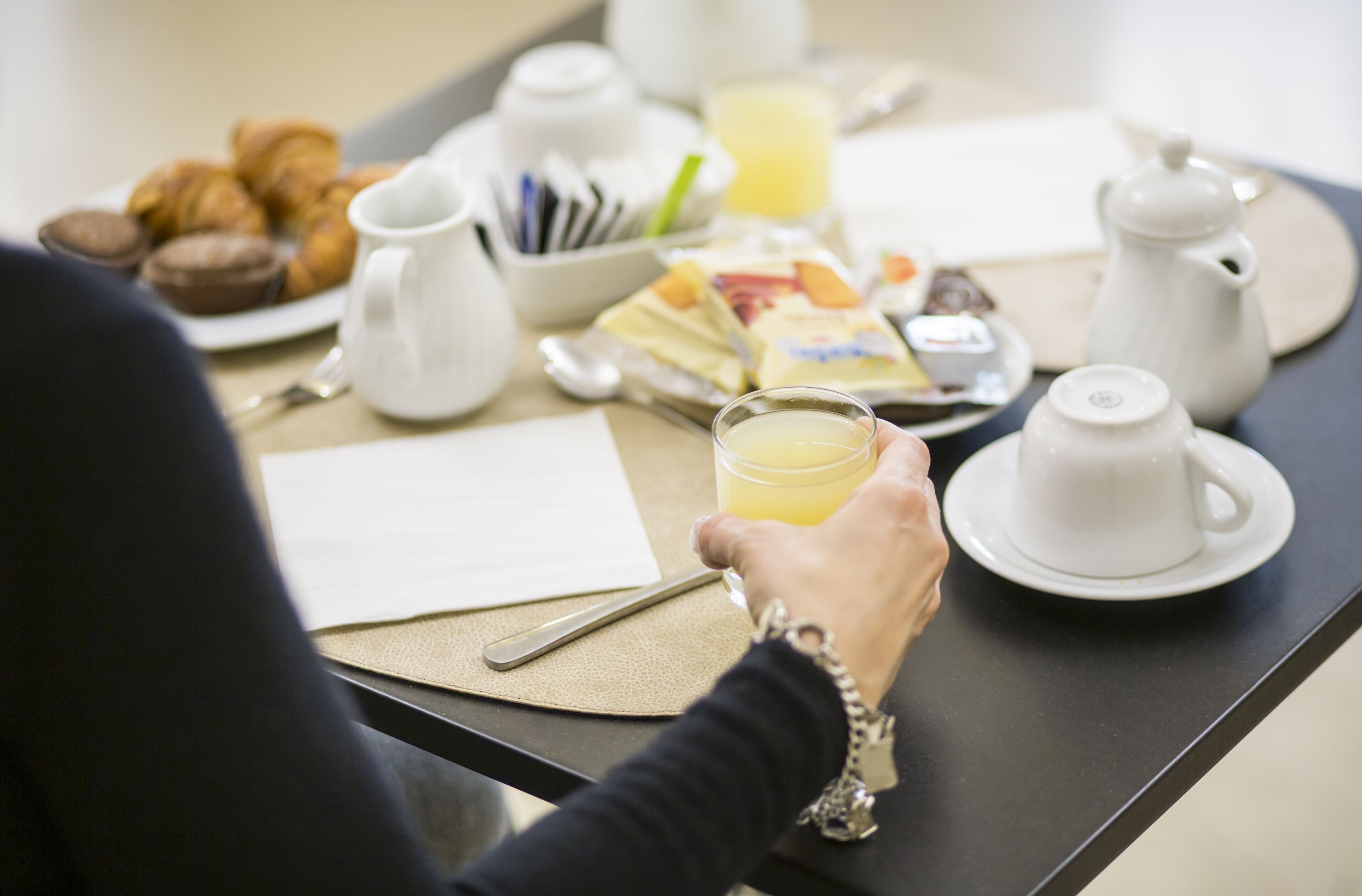 Uma mesa de café da manhã com croissants, uma tábua de frutas, um jarro de suco de laranja e uma chaleira.