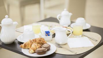 Una tavola imbandita con croissant, muffin, un boccale, un teiera, una tazza e un bicchiere di succo d'arancia.