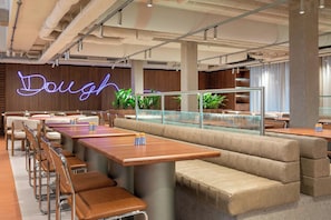 A modern restaurant with booth seating, a neon sign reading "Dough," and a glass railing overlooking the dining area.