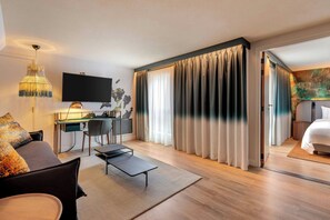 A modern hotel room with a desk, a bed, a TV, and a large window with curtains.
