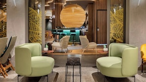 Un interior modern amb dues butaques verdes, una zona de bar i panells decoratius de fusta.