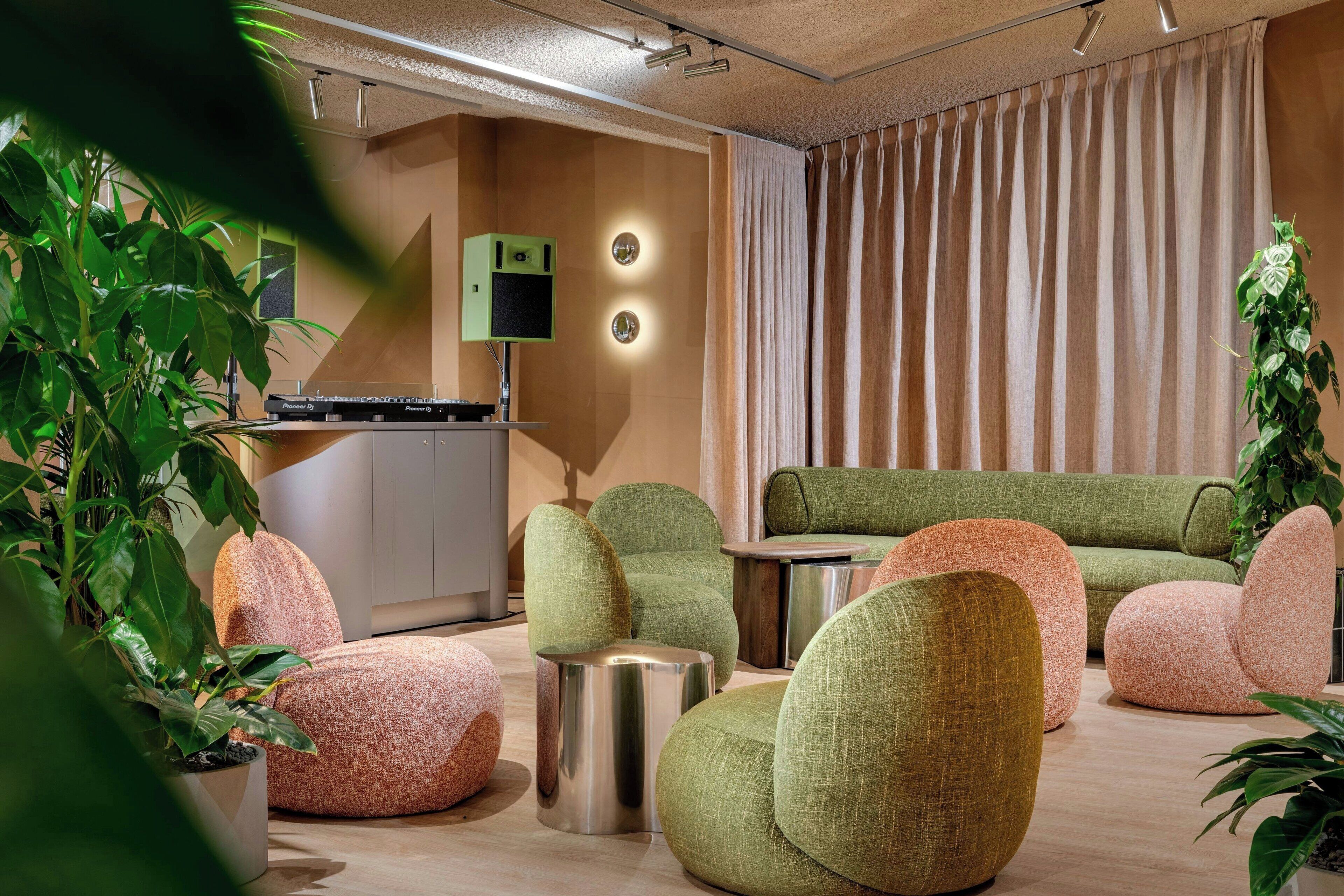 A modern living room with green and pink upholstered furniture, a flat-screen TV, and a kitchen area.