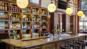 A bar area with wooden shelves stocked with bottles, glasses, and a bar counter with stools.