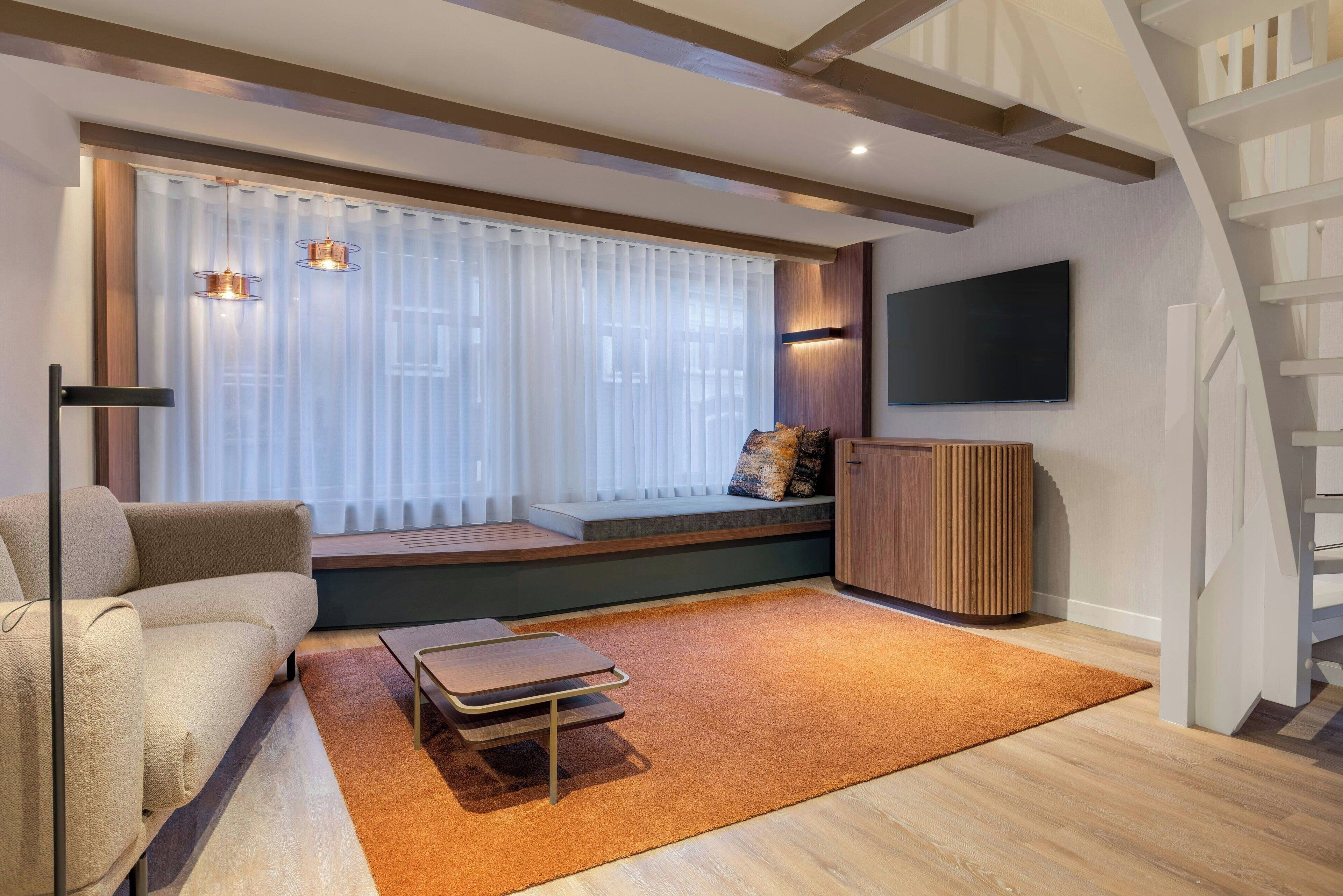 A modern living room with a sofa, a coffee table, a TV mounted on the wall, and a staircase.