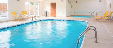 Una piscina interior con agua azul cristalina, rodeada de sillas de descanso amarillas y blancas, y un suelo de baldosas.