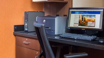 A hotel room with a desk, a desktop computer, a printer, and a chair.