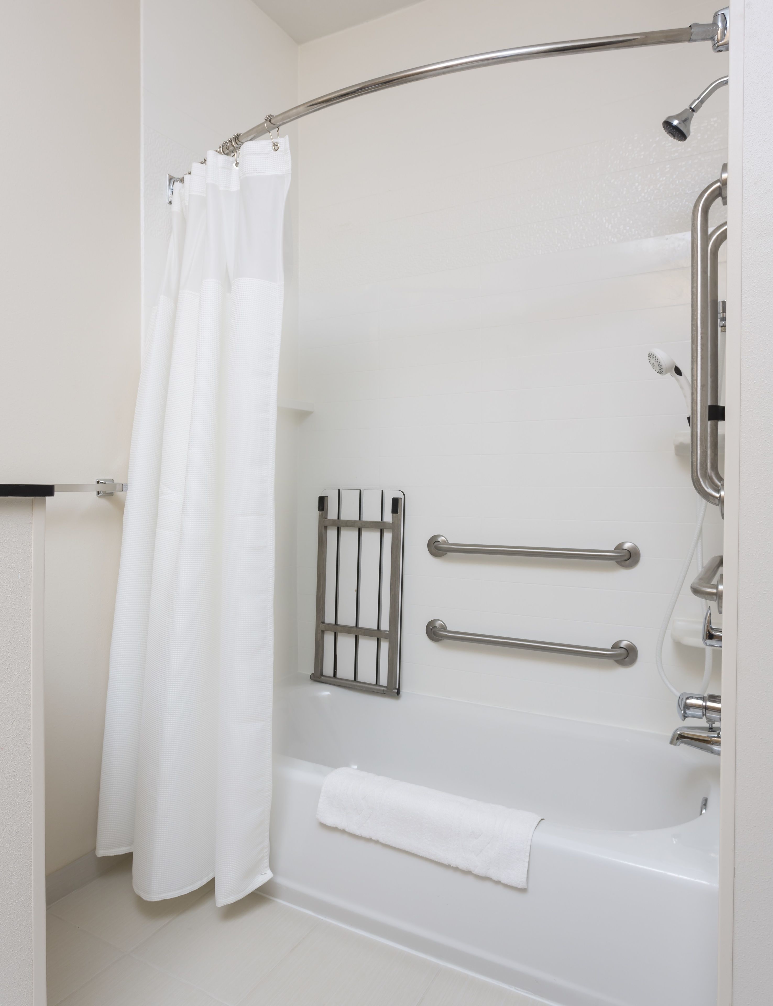Une salle de bain moderne dotée d’une douche à l’italienne, de barres d’appui, d’un porte-serviettes et d’un rideau de douche.