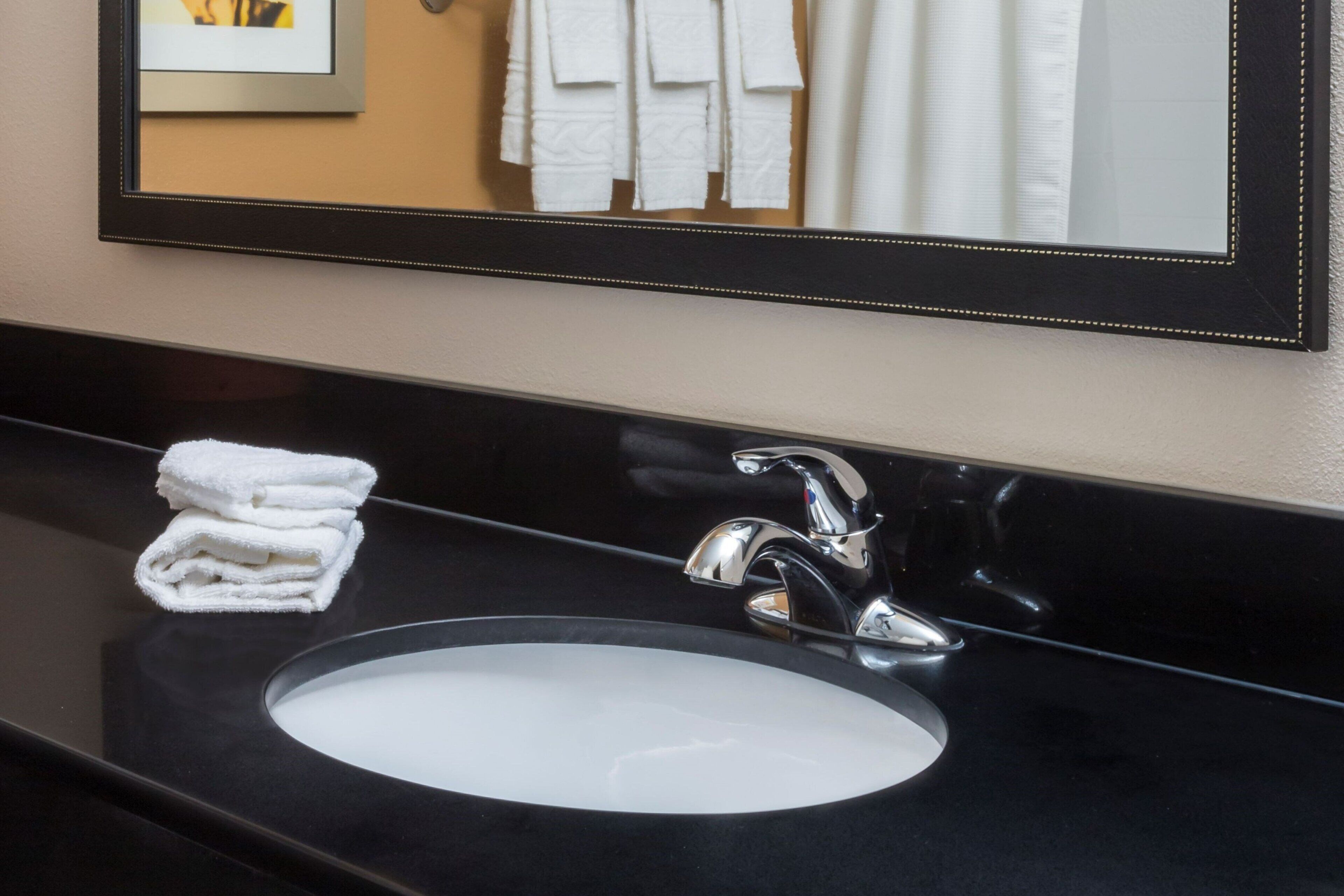 A bathroom with a black countertop, a white sink, and a mirror with a black frame.