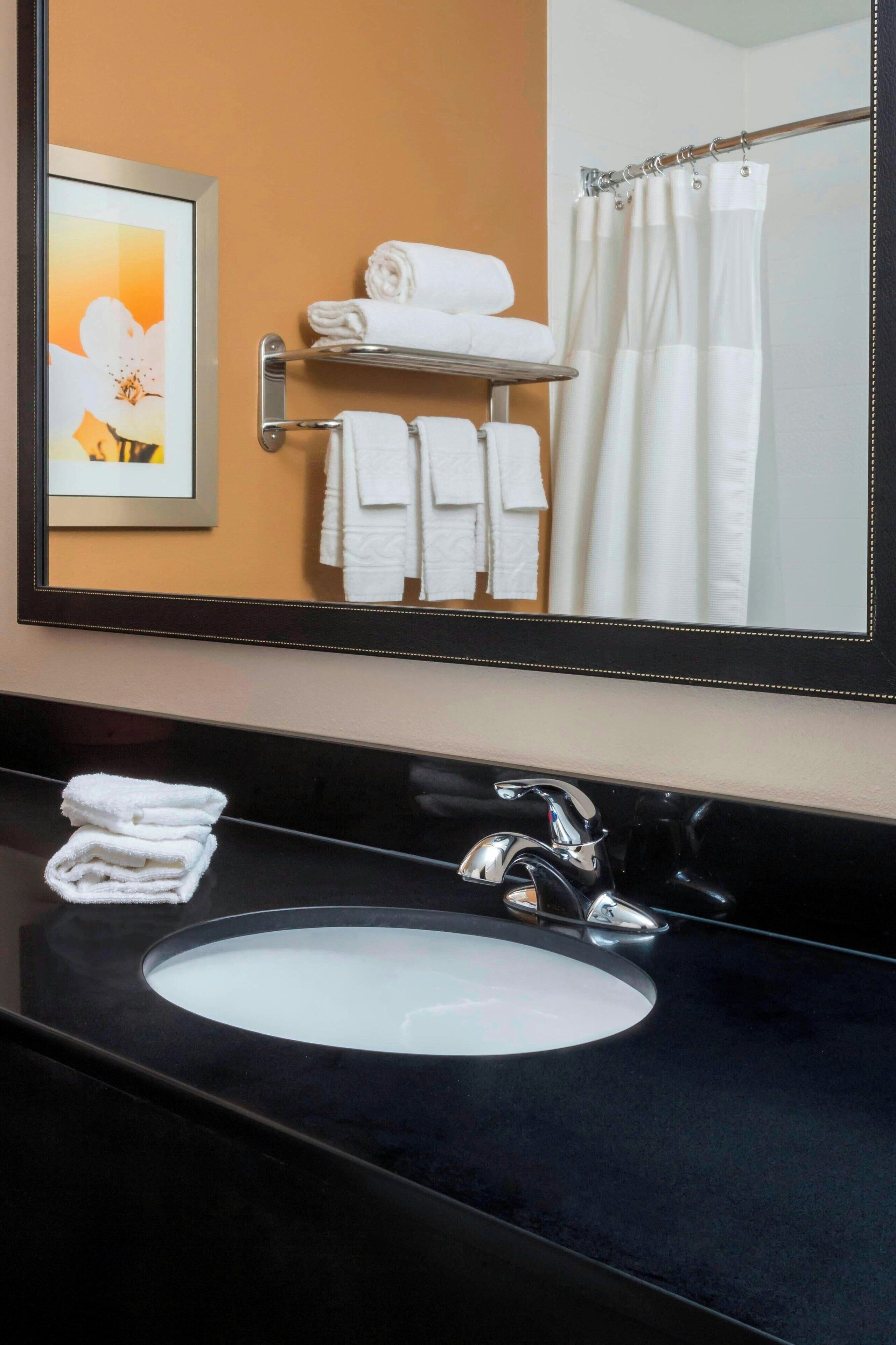 A bathroom with a black sink, a mirror, a framed picture, and a towel rack with folded towels.