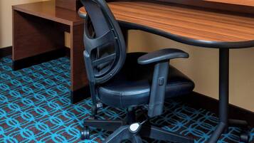 Une chambre d’hôtel équipée d’un bureau, d’une chaise, d’une télévision et d’un tapis à motifs géométriques.