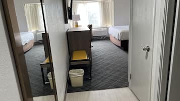 A hotel room with a bed, a desk, a chair, a mirror, a window, and a door.