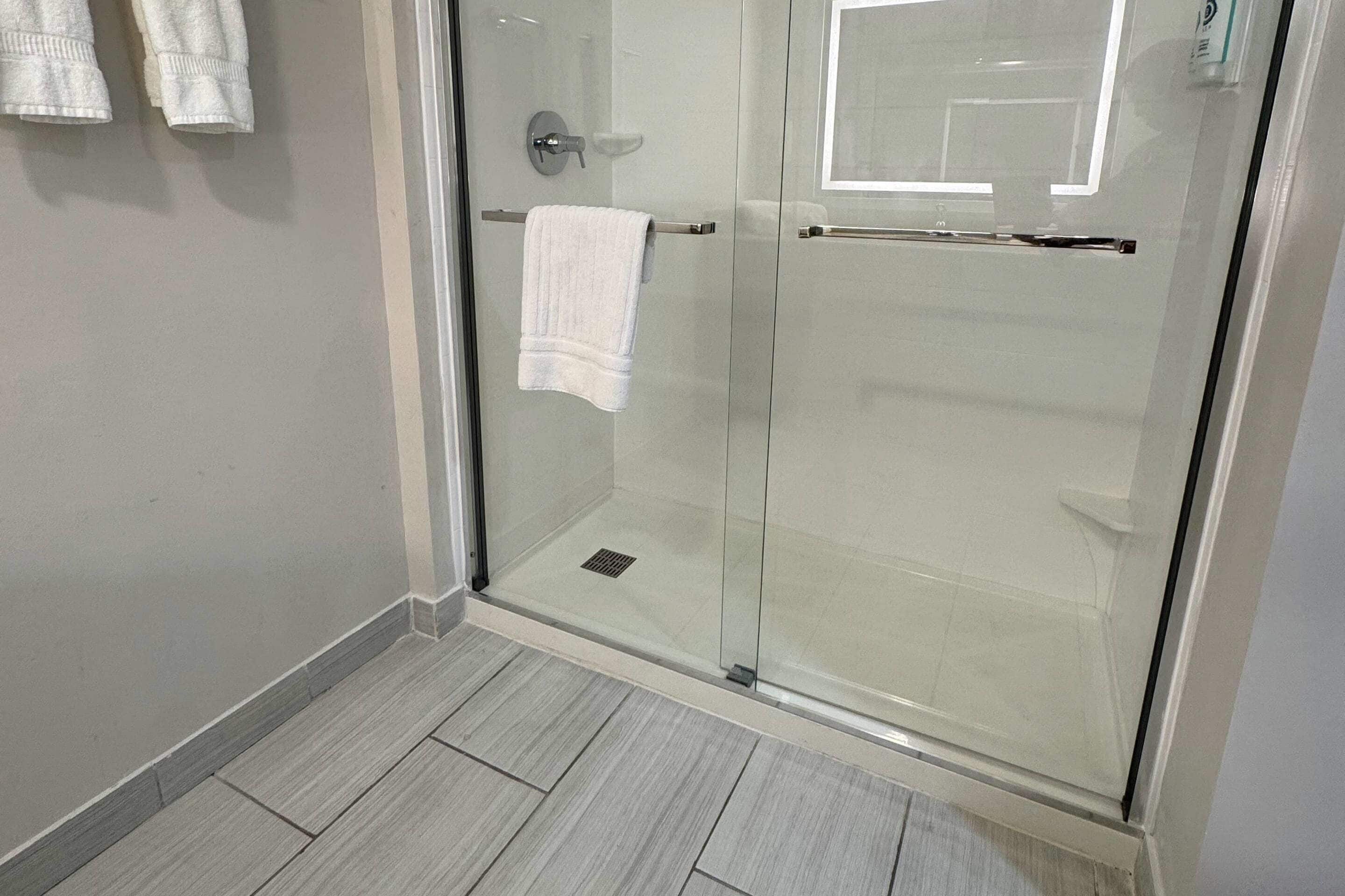 Un baño moderno con cabina de ducha de vidrio, un perchero con dos toallas y suelo de baldosas.