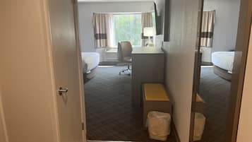 Une chambre d’hôtel avec deux lits, un bureau, une chaise, une petite table et une poubelle.