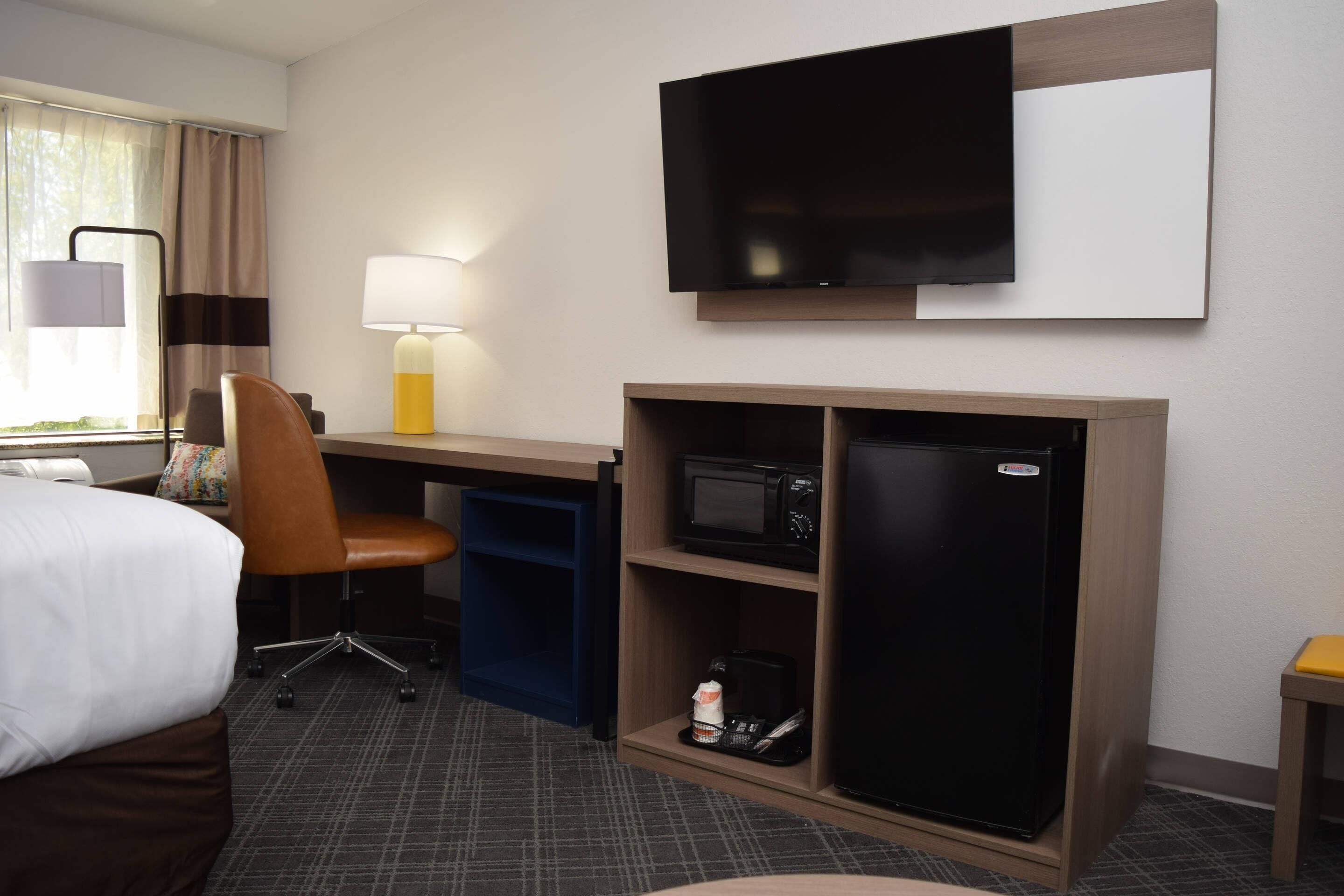 Habitación de hotel con cama, escritorio, silla, televisión, microondas y refrigerador.