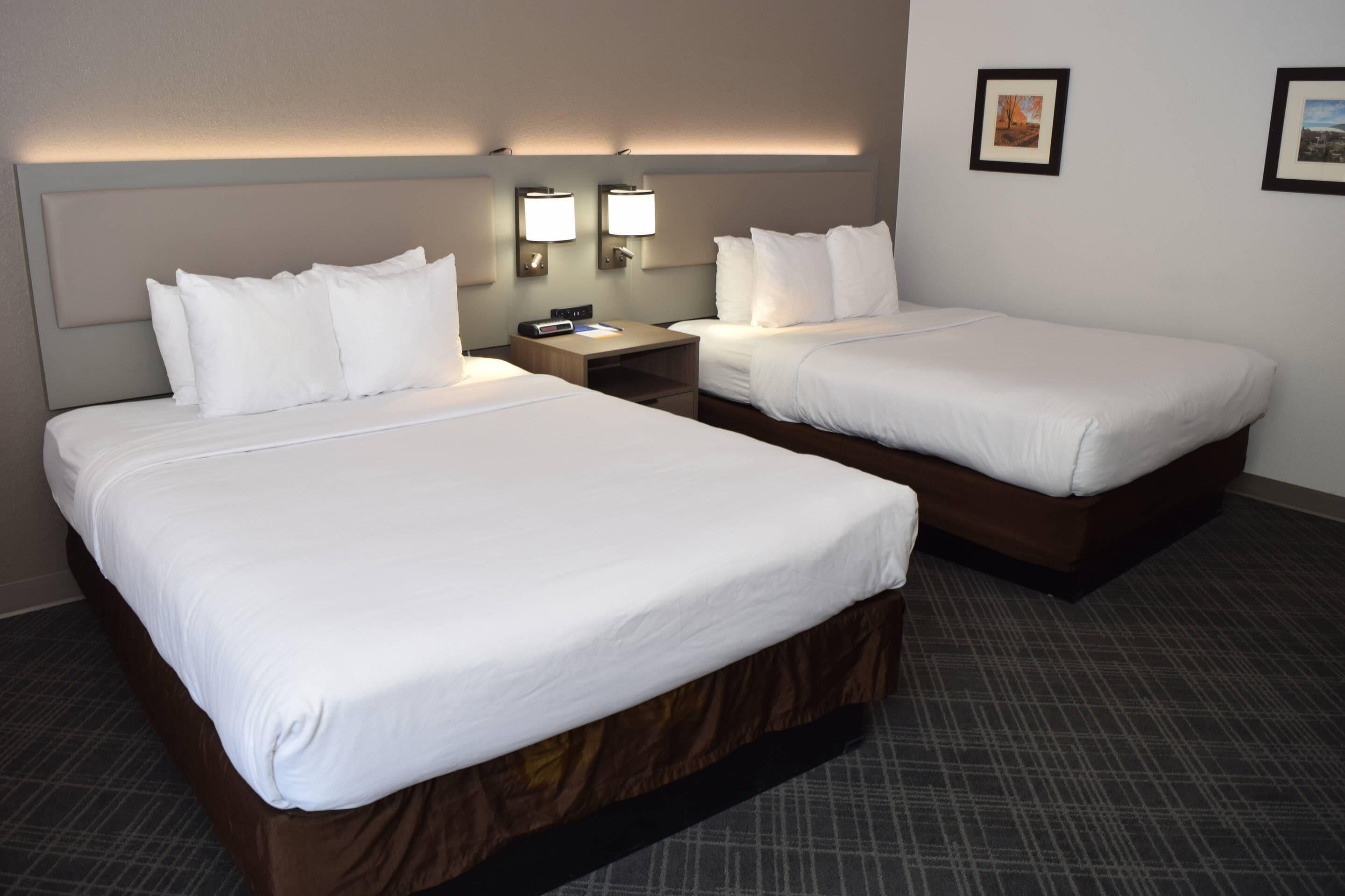 A hotel room with two beds, a nightstand, and wall-mounted lamps.