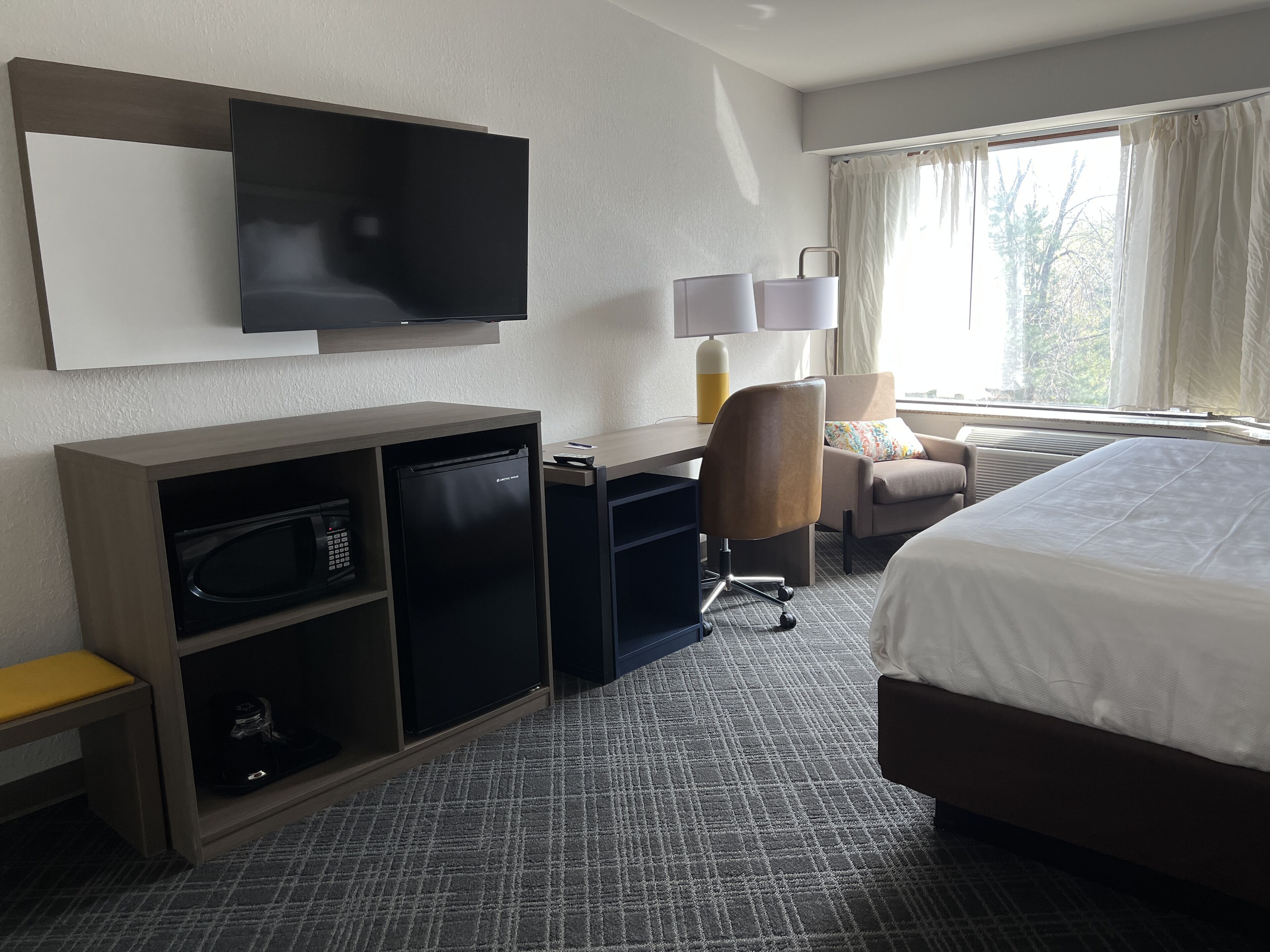 Ein Hotelzimmer mit einem Bett, einem Schreibtisch mit Computer, einem an der Wand montierten Fernseher, einer Mikrowelle und einem kleinen Kühlschrank.