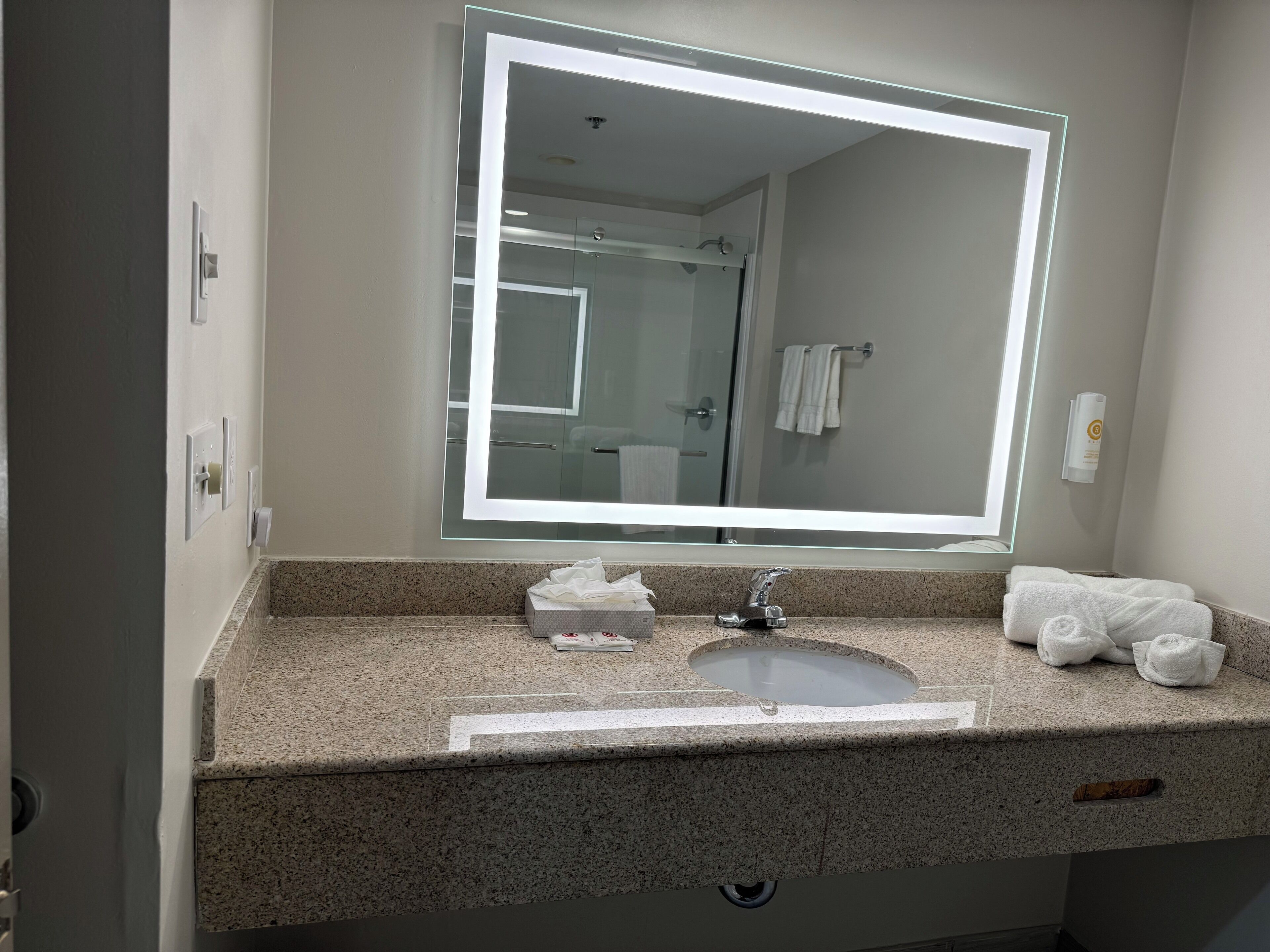 Une salle de bain avec un comptoir en granit, un lavabo, un miroir avec un éclairage intégré et un porte-serviettes avec des serviettes.