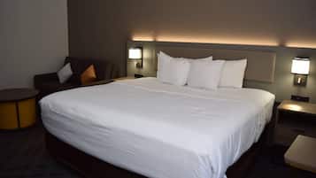 A hotel room with a large bed, two bedside tables, a small round table, and a sofa with cushions.
