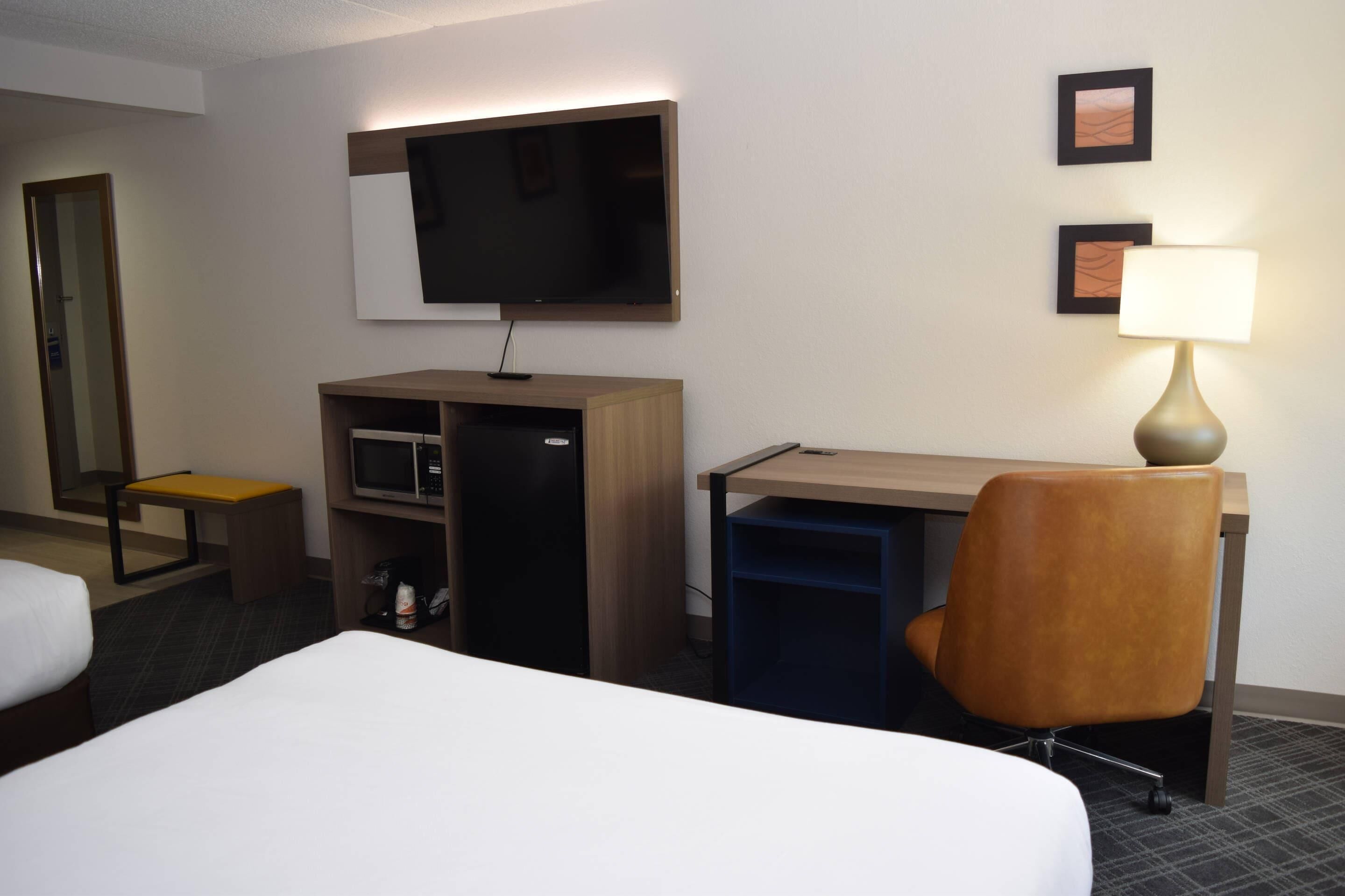 Une chambre d’hôtel équipée d’un lit, d’un bureau, d’une chaise, d’une télévision, d’une lampe et d’un mini-bar.