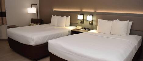 A hotel room with two beds, each with white linens, a nightstand with a lamp, and two wall-mounted light fixtures.